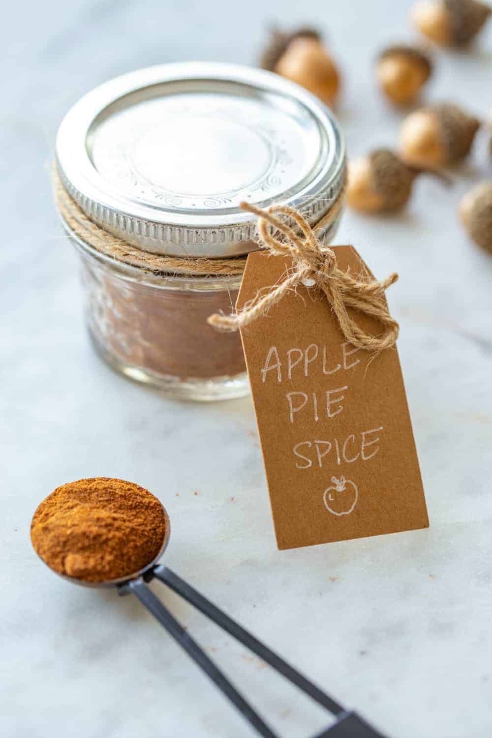 Jar of apple pie spice with a fall gift tag next to a measuring spoon of the spice blend