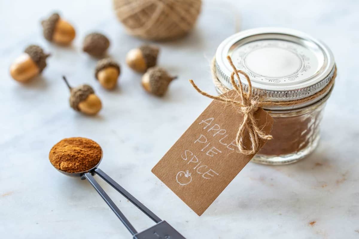 Apple pie spice packaged for gifting in a jar with a tag, next to a ball of twine and a spoon of apple pie spice