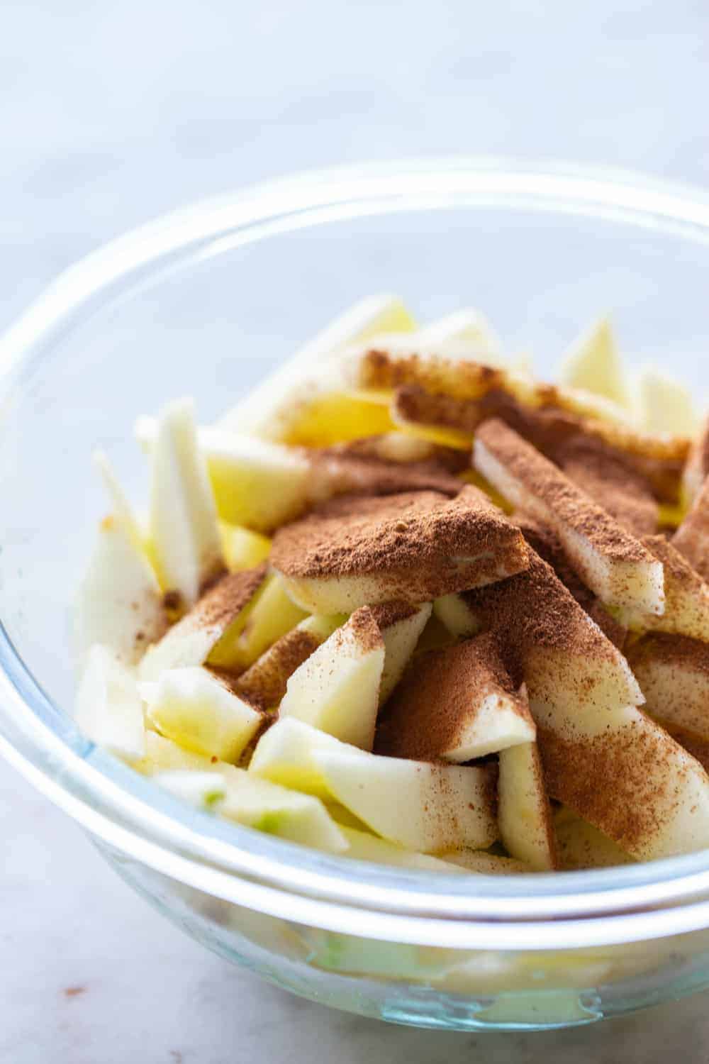 Apple pie spice sprinkled over sliced apples in a glass mixing bowl