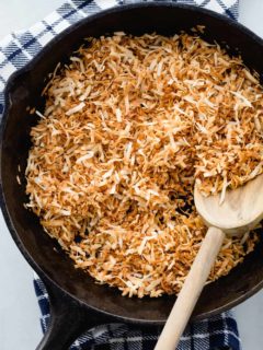Toasted coconut in a cast iron skillet with a wooden spoon