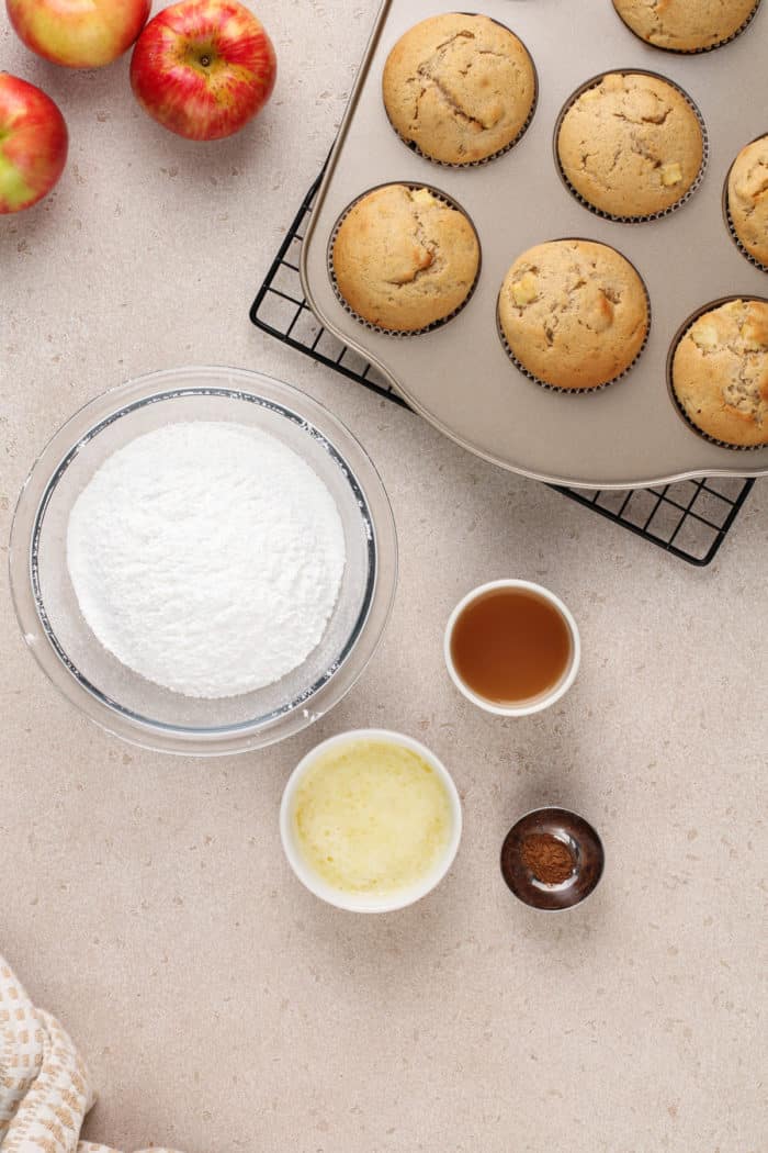 Ingredients for apple cider glaze next to a pan of baked apple cider donut muffins.