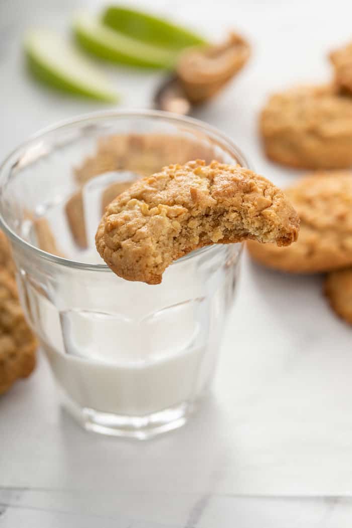Apple peanut butter cookie, with a bite taken out of it, balancing on the edge of a glass of milk