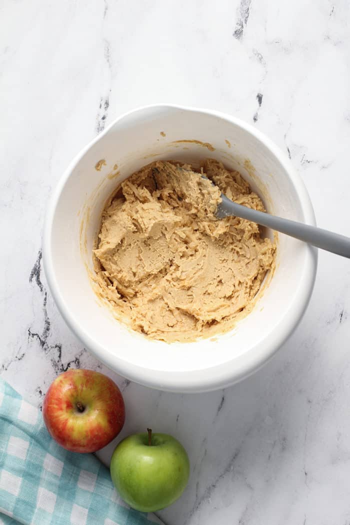 Spatula stirring apple peanut butter cookie dough in a white mixing bowl