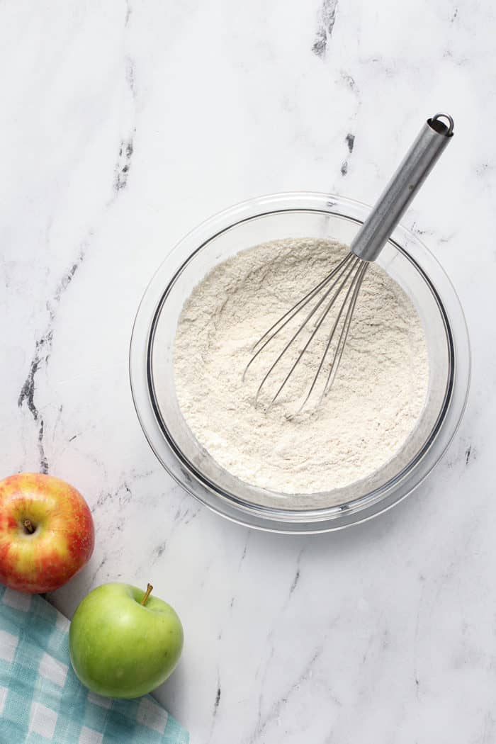 Whisk stirring together the dry ingredients for apple peanut butter cookies in a glass mixing bowl