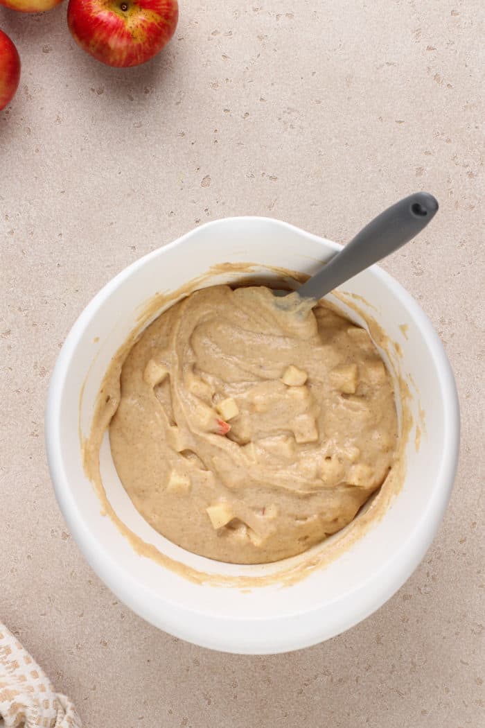 Diced apples mixed into the batter for apple cider donut muffins in a white bowl.