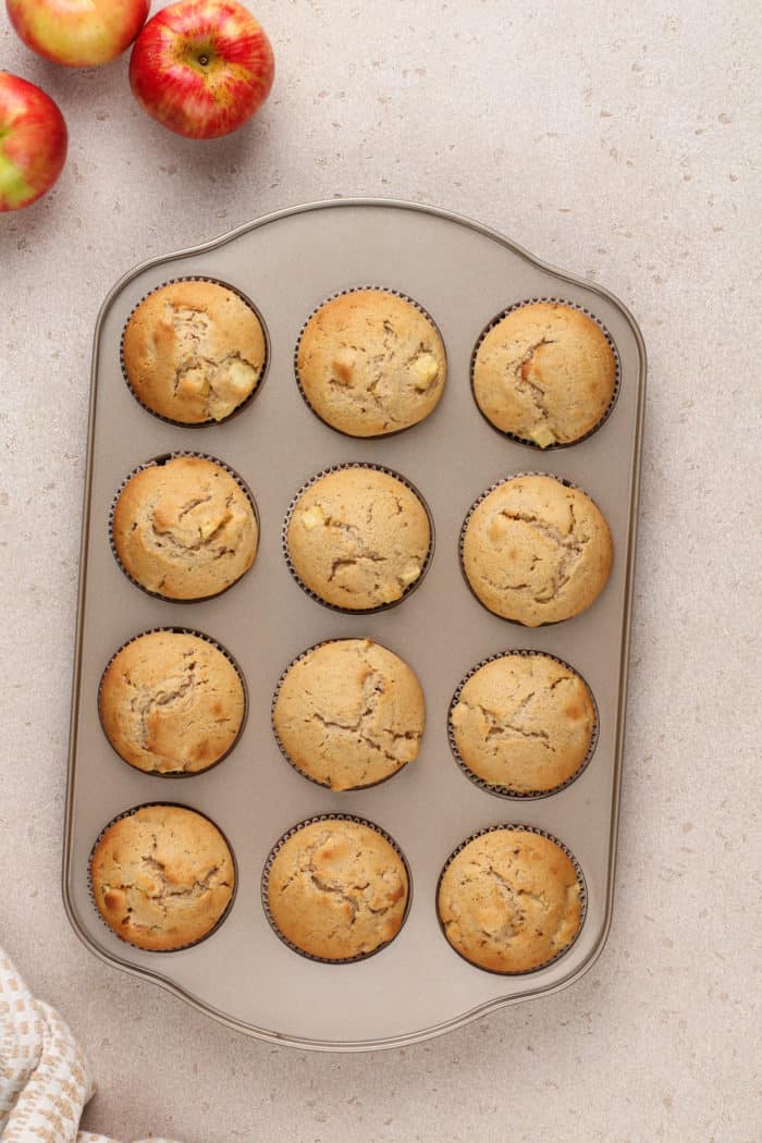 Baked apple cider donut muffins in a muffin tin.