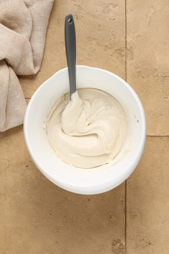 Spatula stirring cream cheese frosting in a white mixing bowl