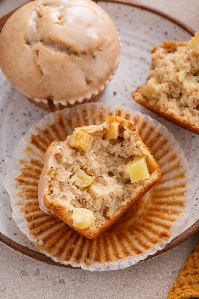 Halved apple cider donut muffin on a plate, showing the chunks of apple in the muffin.