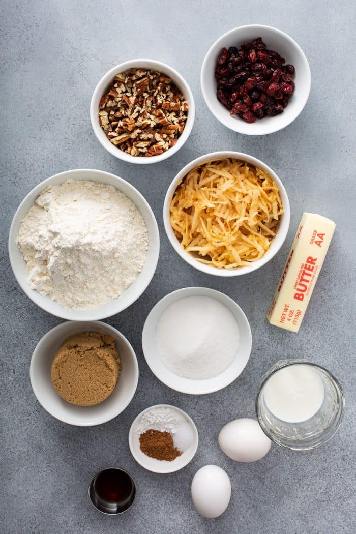 Overhead view of the ingredients for apple pie bread arranged in bowls on a gray countertop