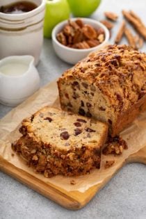 Sliced loaf of apple pie bread on a cutting board with coffee, apples and spices in the background