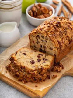Sliced loaf of apple pie bread on a cutting board with coffee, apples and spices in the background