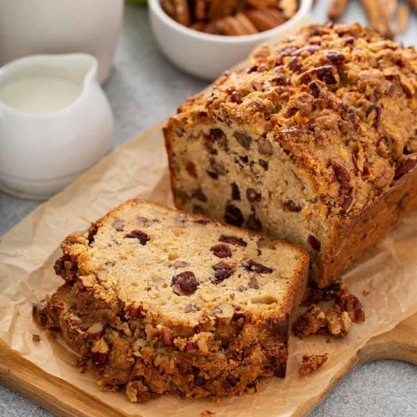 Sliced loaf of apple pie bread on a cutting board with coffee, apples and spices in the background