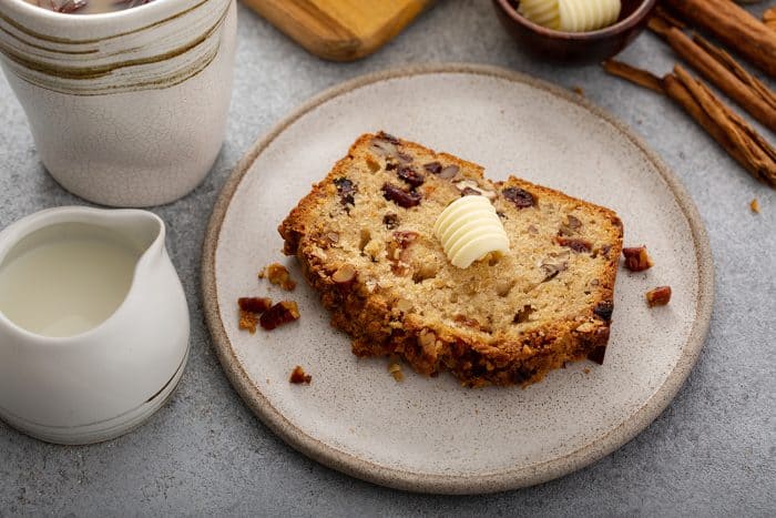 Slice of apple pie bread topped with a pat of butter on a cream plate