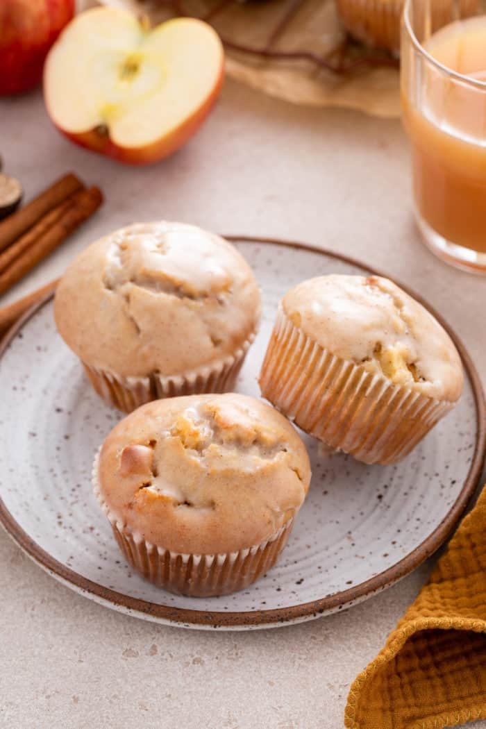 Three apple cider donut muffins arranged on a speckled plate.