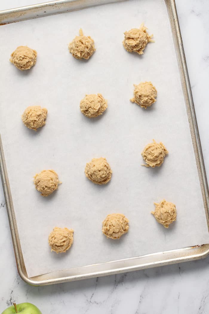 Spoonfuls of apple peanut butter cookie dough portioned on a parchment-lined cookie sheet
