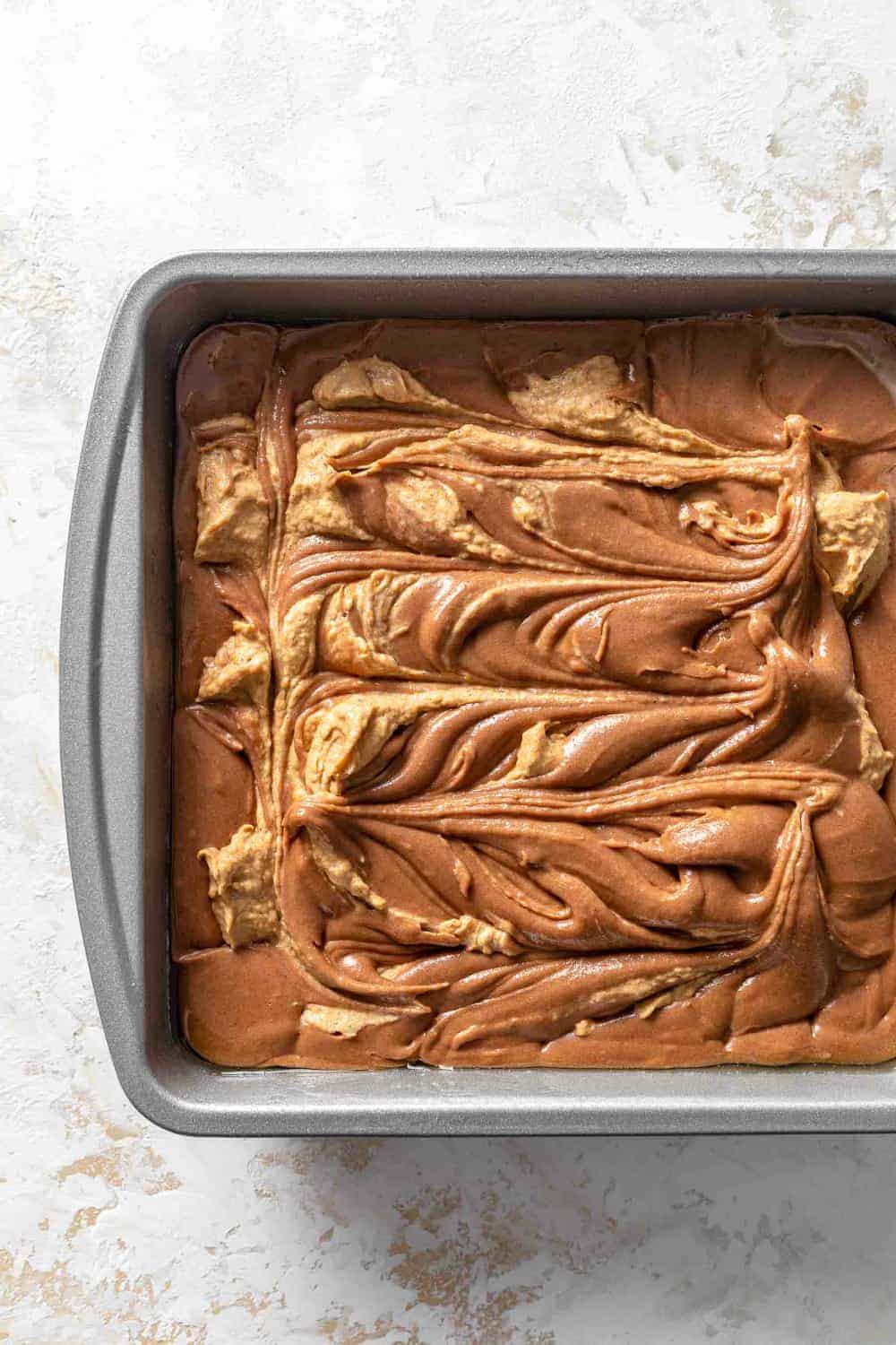 Brownie batter swirled with a pumpkin cream cheese mixture in a pan, ready to bake
