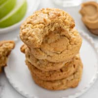 5 apple peanut butter cookies stacked on a white plate. The top cookie has a bite taken out of it