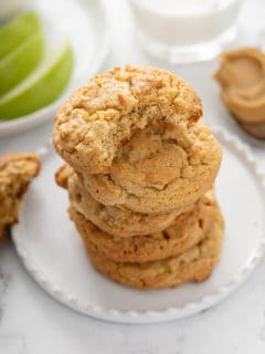 5 apple peanut butter cookies stacked on a white plate. The top cookie has a bite taken out of it