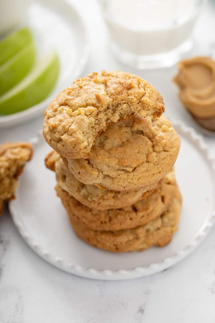 5 apple peanut butter cookies stacked on a white plate. The top cookie has a bite taken out of it