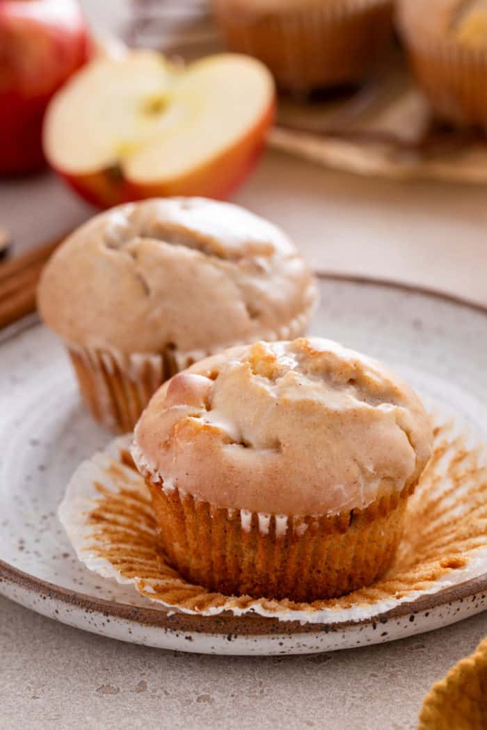Two apple cider donut muffins on a plate. The muffin in front is unwrapped.