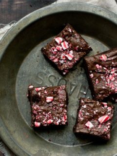Four dark chocolate candy cane brownies in a metal pie tin on a wood table