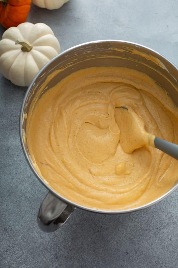 Spatula folding pumpkin cheesecake filling in a metal mixing bowl