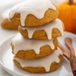 Four iced pumpkin cookies stacked on a white plate