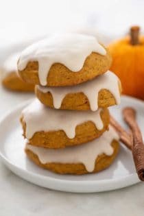 Four iced pumpkin cookies stacked on a white plate