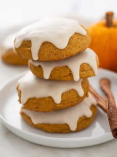 Four iced pumpkin cookies stacked on a white plate