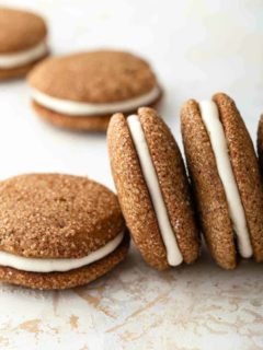 Pumpkin molasses sandwich cookies arranged on a countertop, some propped on their sides