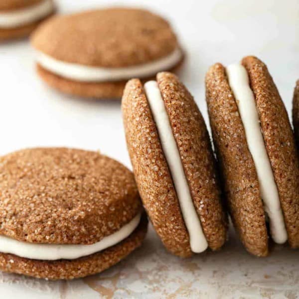 Pumpkin molasses sandwich cookies arranged on a countertop, some propped on their sides