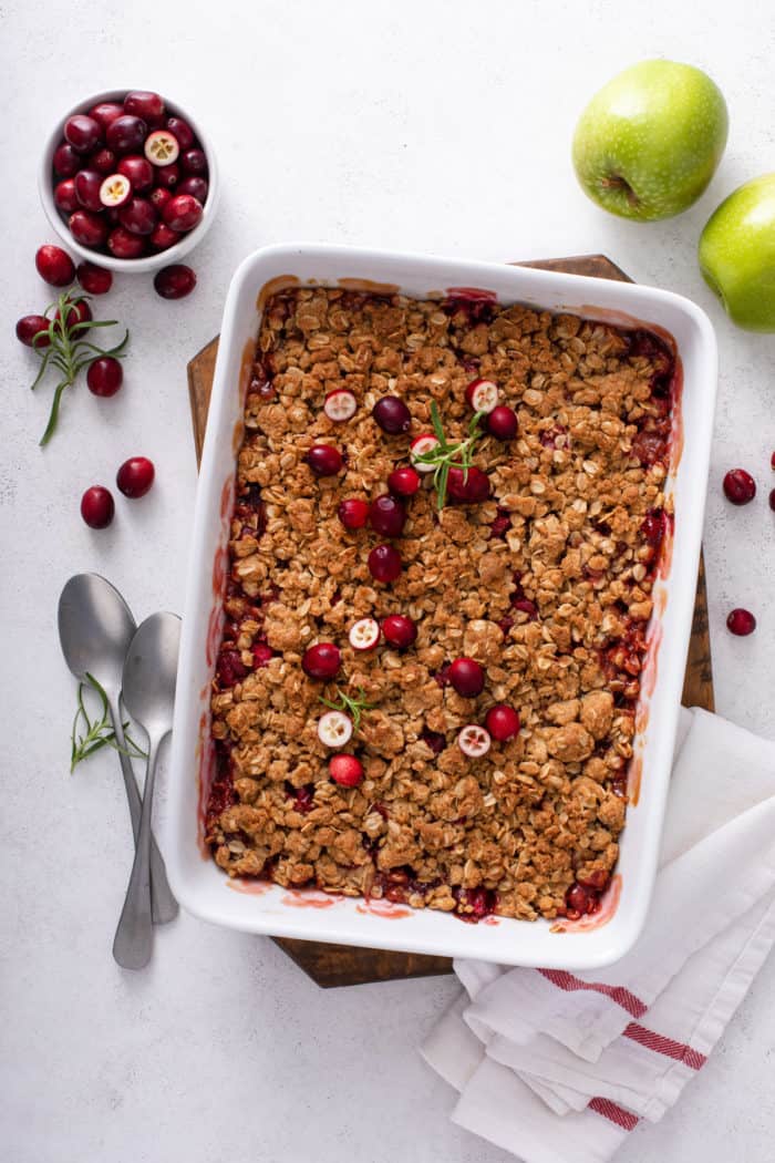 Overhead view of baked cranberry apple crisp in a white baking dish, set on a wooden trivet on a countertop.