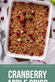 Overhead view of baked cranberry apple crisp in a white baking dish, set on a wooden trivet on a countertop. Text overlay includes recipe name.