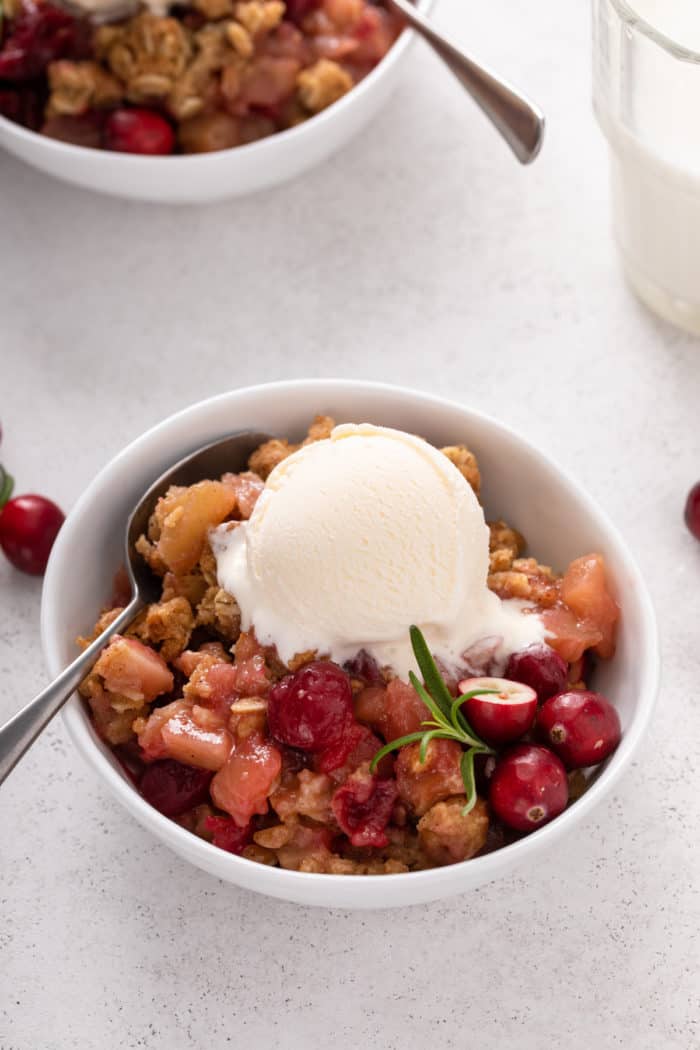 White bowl filled with cranberry apple crisp, topped with a scoop of vanilla ice cream.