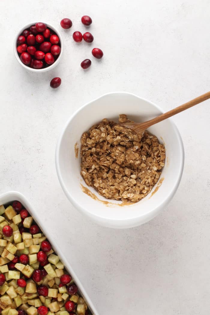 Topping for cranberry apple crisp being stirred with a wooden spoon in a white mixing bowl.