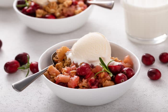 Cranberry apple crisp topped with a scoop of vanilla ice cream in a white bowl.