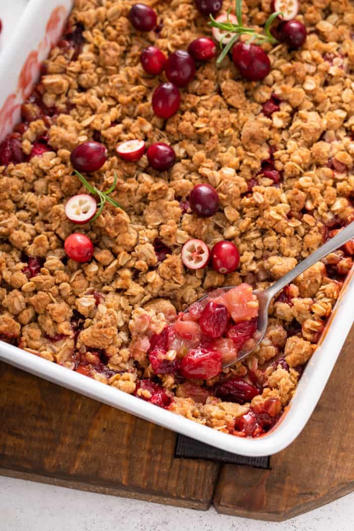 Spoon taking a spoonful of cranberry apple crisp out of the corner of a white baking dish.