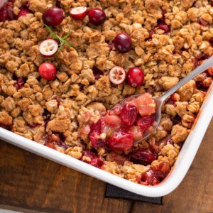 Spoon picking up a serving of cranberry apple crisp from the baking dish.