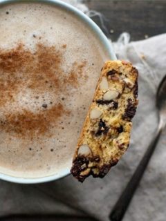 A chocolate cherry almond biscotti sitting on a mug of cappuccino