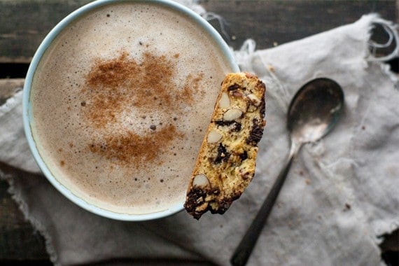 A chocolate cherry almond biscotti sitting on a mug of cappuccino