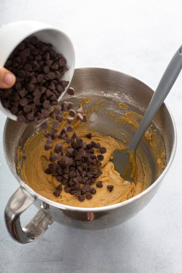 Chocolate chips being added to dough for blondies in a metal mixing bowl