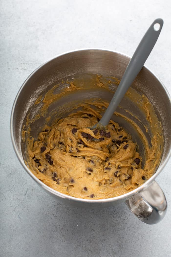 Spatula folding chocolate chips into blondie batter in a metal mixing bowl
