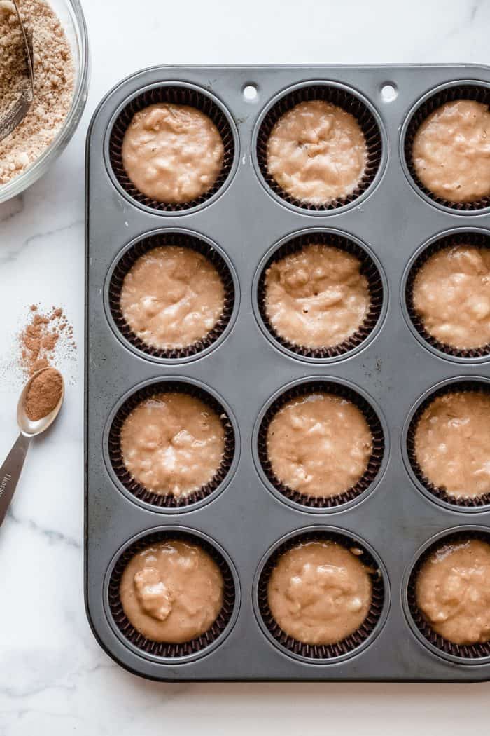 Muffin tin filled with batter for banana crumb muffins, set on a marble countertop