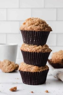 Three banana crumb muffins stacked on top of each other on a marble countertop