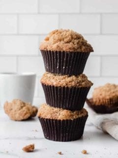 Three banana crumb muffins stacked on top of each other on a marble countertop