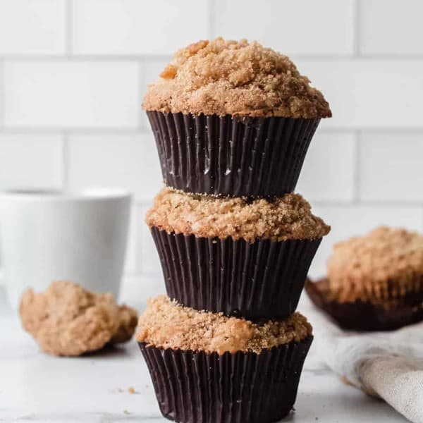 Three banana crumb muffins stacked on top of each other on a marble countertop