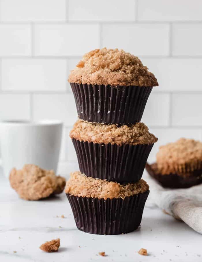 Three banana crumb muffins stacked on top of each other on a marble countertop