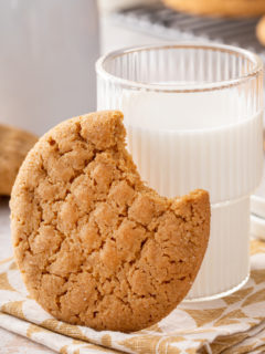Honey peanut butter cookie with a bite taken from it leaning against a glass of milk.