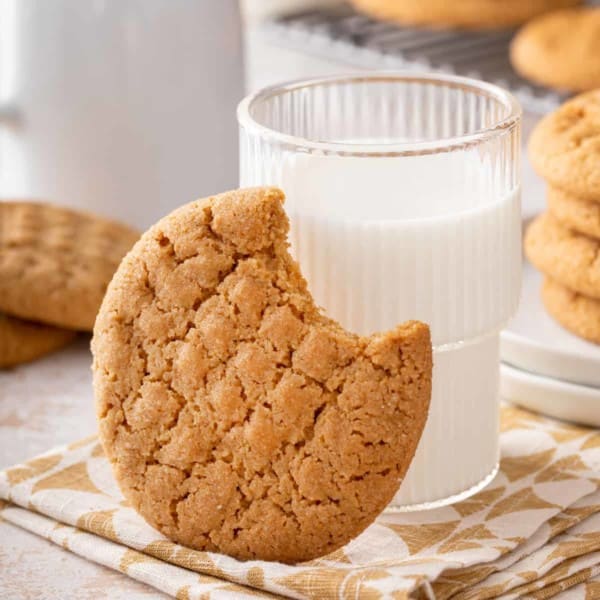 Honey peanut butter cookie with a bite taken from it leaning against a glass of milk.