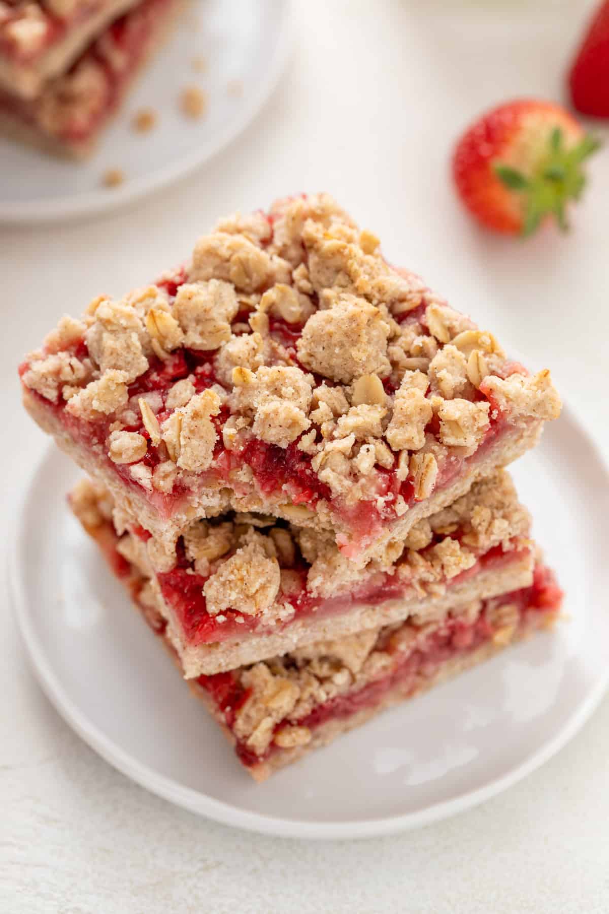 Three strawberry oatmeal bars stacked on a plate with a bite taken from a corner of the top bar.